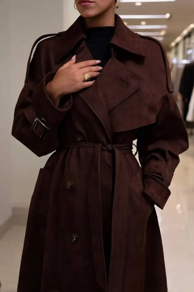 Luxurious fall winter outfits, oversized brown trench coat with collar, cinched waist belt, layered gold jewelry, rings and bracelets, styled with black underlayer for elegant cold weather styling