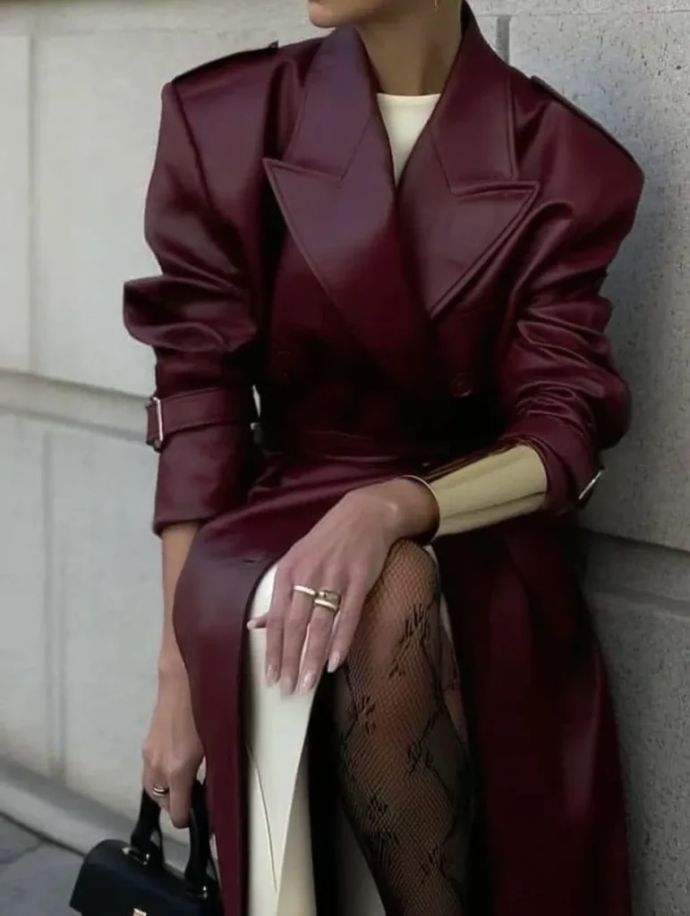 Sophisticated classy fall outfits, luxurious burgundy leather trench coat, cream turtleneck sweater, lace tights, gold statement rings, and black handbag for elegant autumn styling inspiration