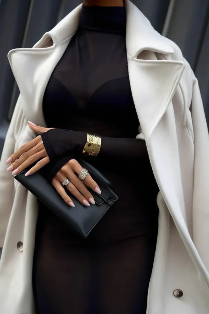 Sophisticated fall winter outfits, luxe layering with beige oversized trench coat over black sweater dress, and black leather pouch bag for upscale autumn fashion