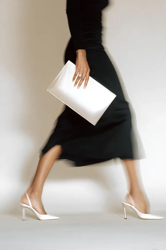 Chic skirt outfits winter, monochromatic black ensemble with sleek satin midi-length skirt and black tank top, white pointy-toe pumps and white envelope clutch for polished seasonal style