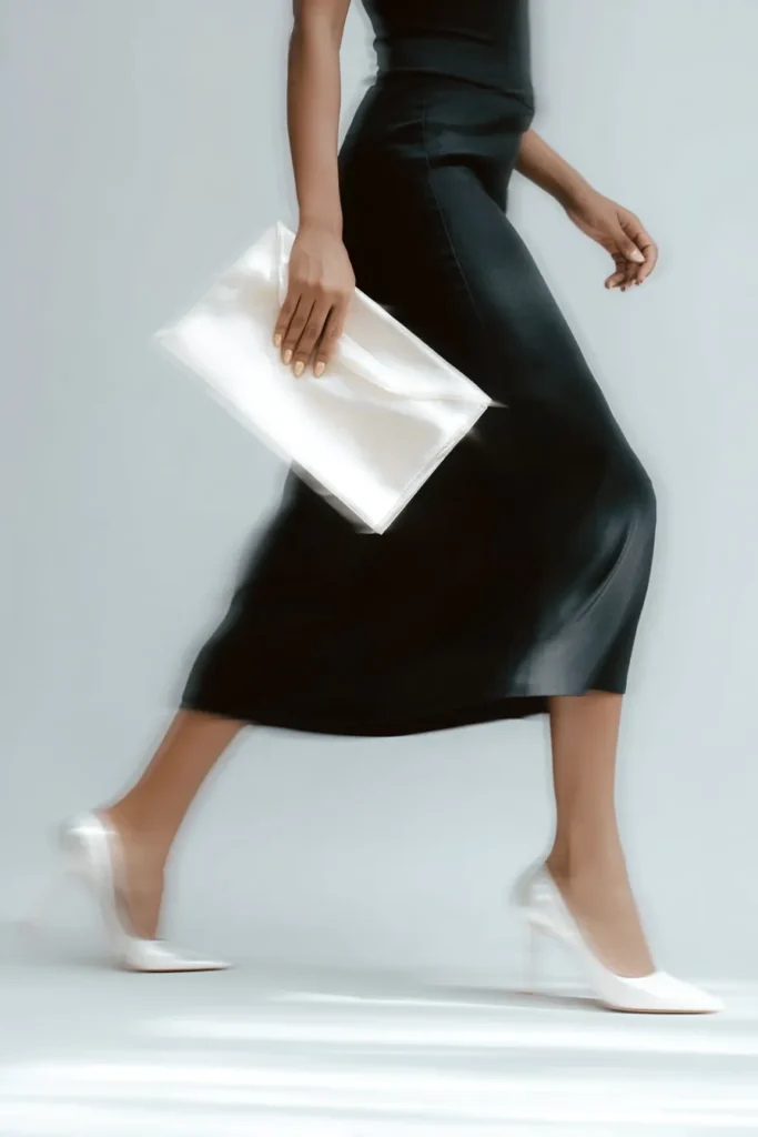 Skirt outfits winter, elegant black midi skirt with matching black sleeveless top, styled with white stiletto heels and white leather clutch bag for sophisticated cold weather evening styling