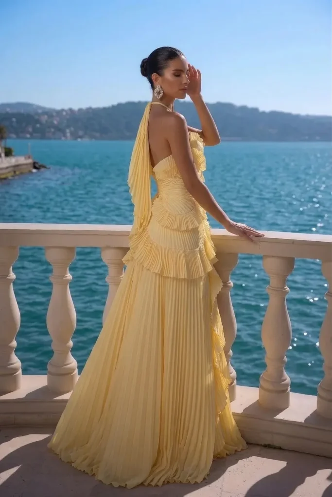 Chic butter yellow trendy wedding guest dress, halter neckline, cascading ruffle panels and pleated maxi skirt, accessorized with statement earrings for luxury coastal wedding look