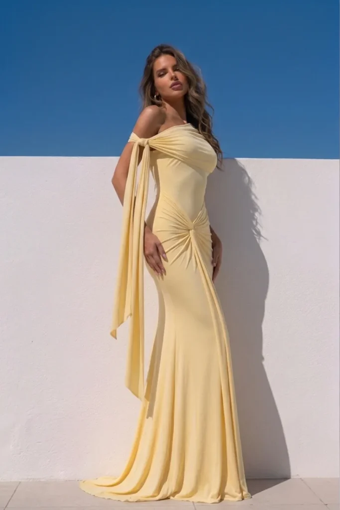 Elegant butter yellow classy wedding guest dress, one-shoulder neckline with a chic knot detail, ruched twist waist, mermaid skirt, sophisticated summer wedding guest outfit with old money appeal
