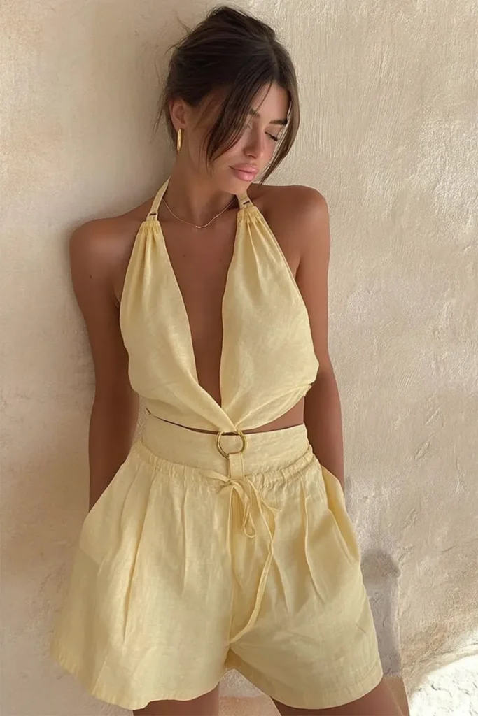 Trendy lemon chic spring outfits, soft yellow halter waistcoat and tailored shorts with button detail, accessorized with bold gold ring jewelry for effortless sophistication