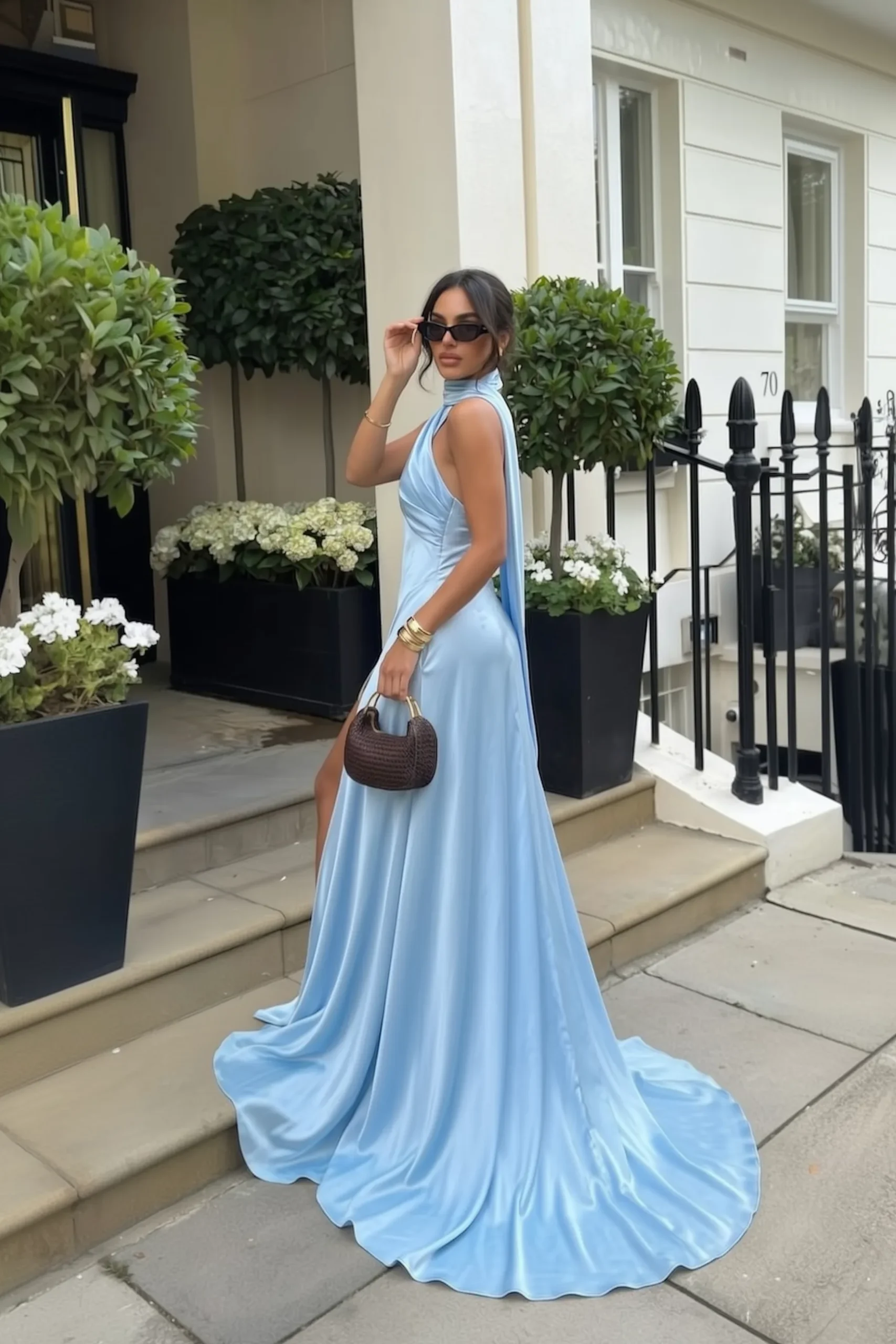 Light blue wedding guest dress, stunning blue satin halter neck maxi gown with a glamorous and elegant train, styled with cat-eye sunglasses, and a chic woven mini bag, breathtaking wedding fashion