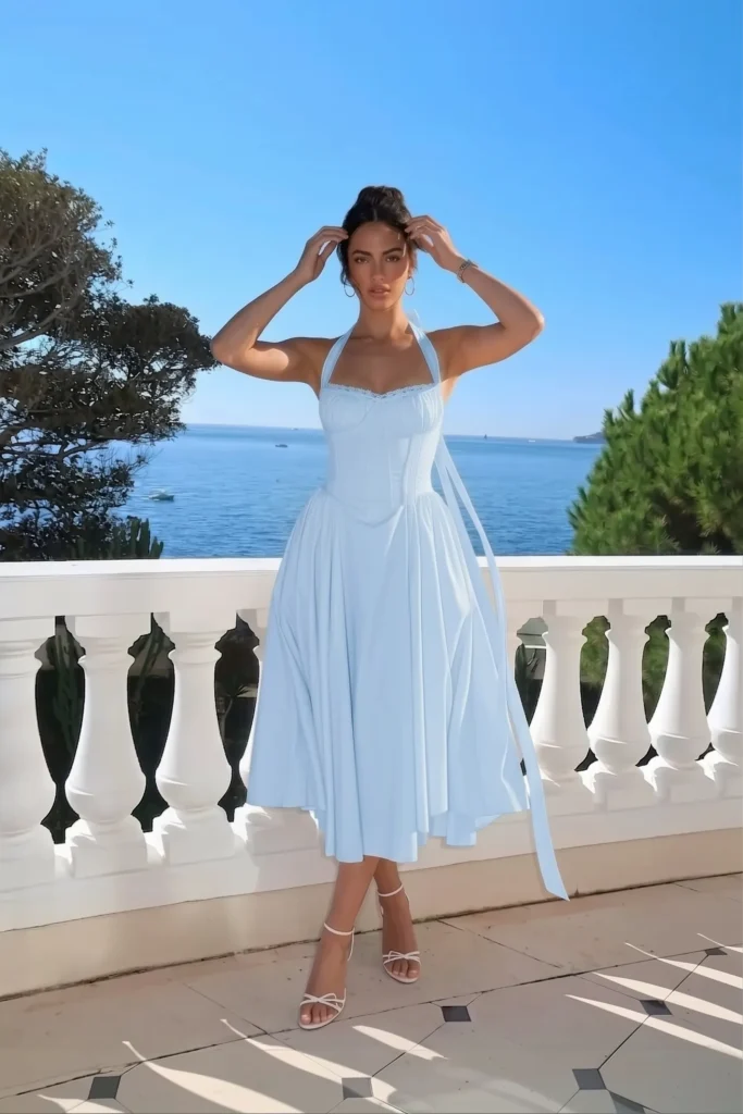 Blue summer birthday outfit, light blue halter neck midi dress, corset bodice, delicate lace trim detail, long ribbon tie, voluminous full tea-length skirt, gold earrings, strappy white heeled sandals