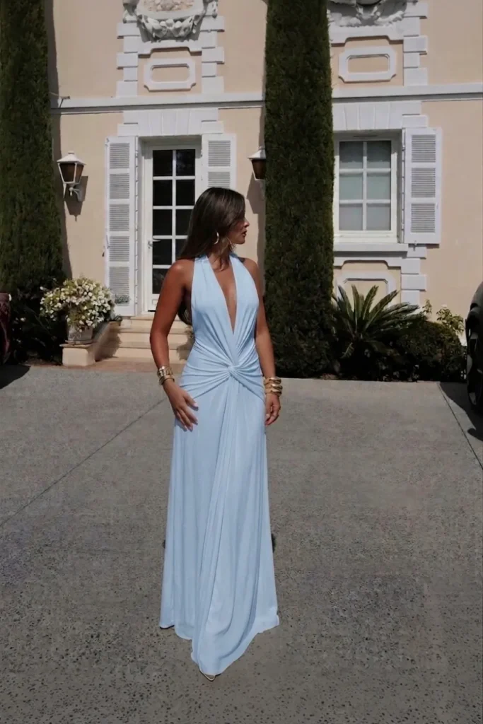 Blue summer night outfit, blue   halter neck maxi dress, twisted knot waist detail and a flowing floor-length skirt with a subtle train, gold  bangles and earrings, outside a beautiful French villa