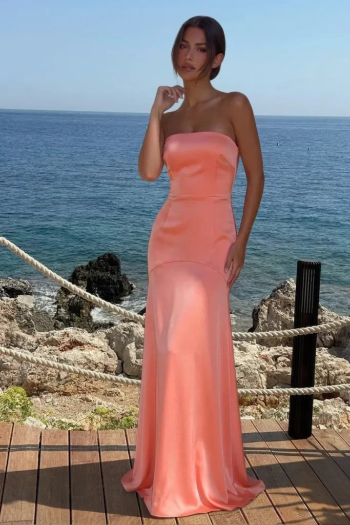 Coral classy wedding guest dress in a sleek strapless satin bandeau style with a fitted bodice, panelled waist detail and flowing floor-length mermaid skirt with a subtle train