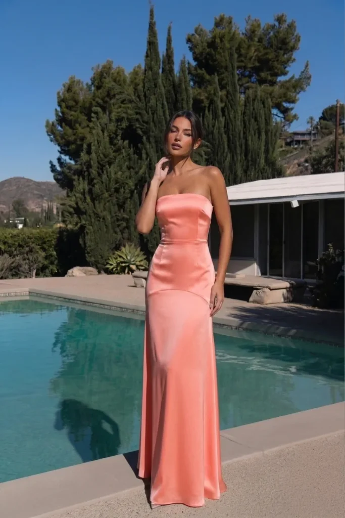 Coral classy wedding guest dress in a sleek strapless satin bandeau style with a straight neckline, structured fitted bodice and a gracefully flared floor-length skirt with a subtle train